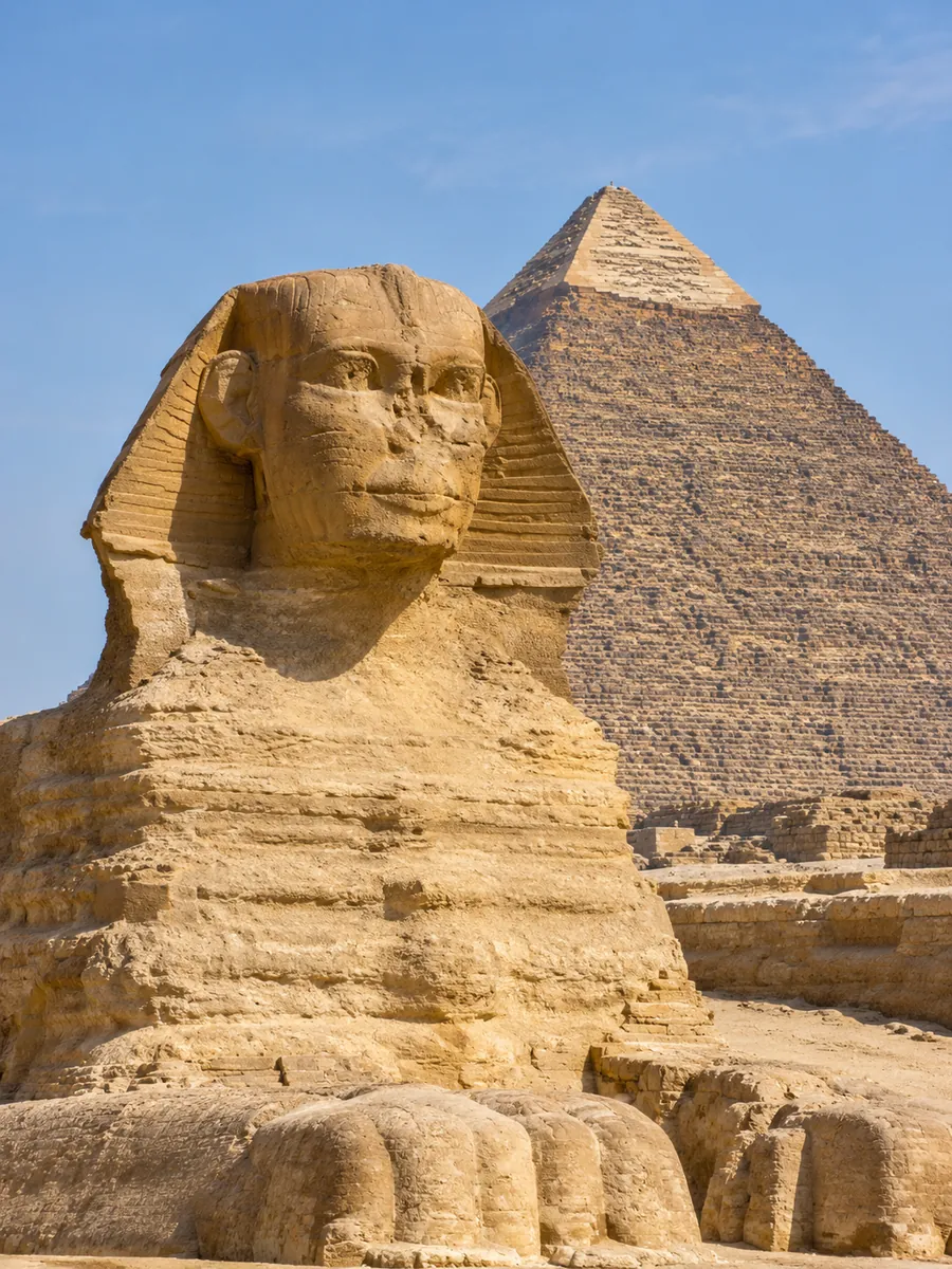 The head of the Great Sphinx with the pyramid of Khafre behind it under a clear sky